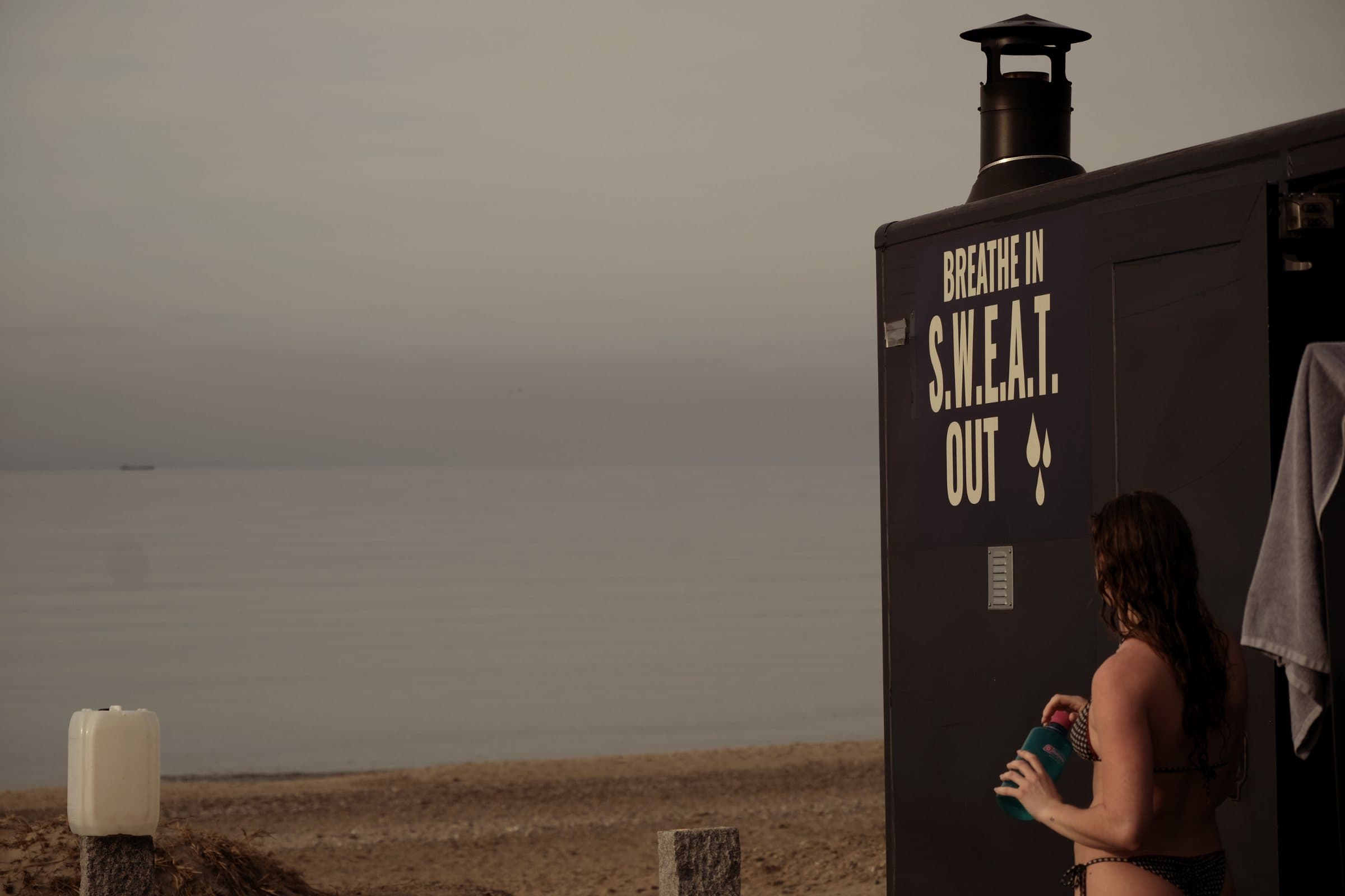Gæst ved saunavognen med teksten Breathe in S.W.E.A.T. out, med havet i baggrunden